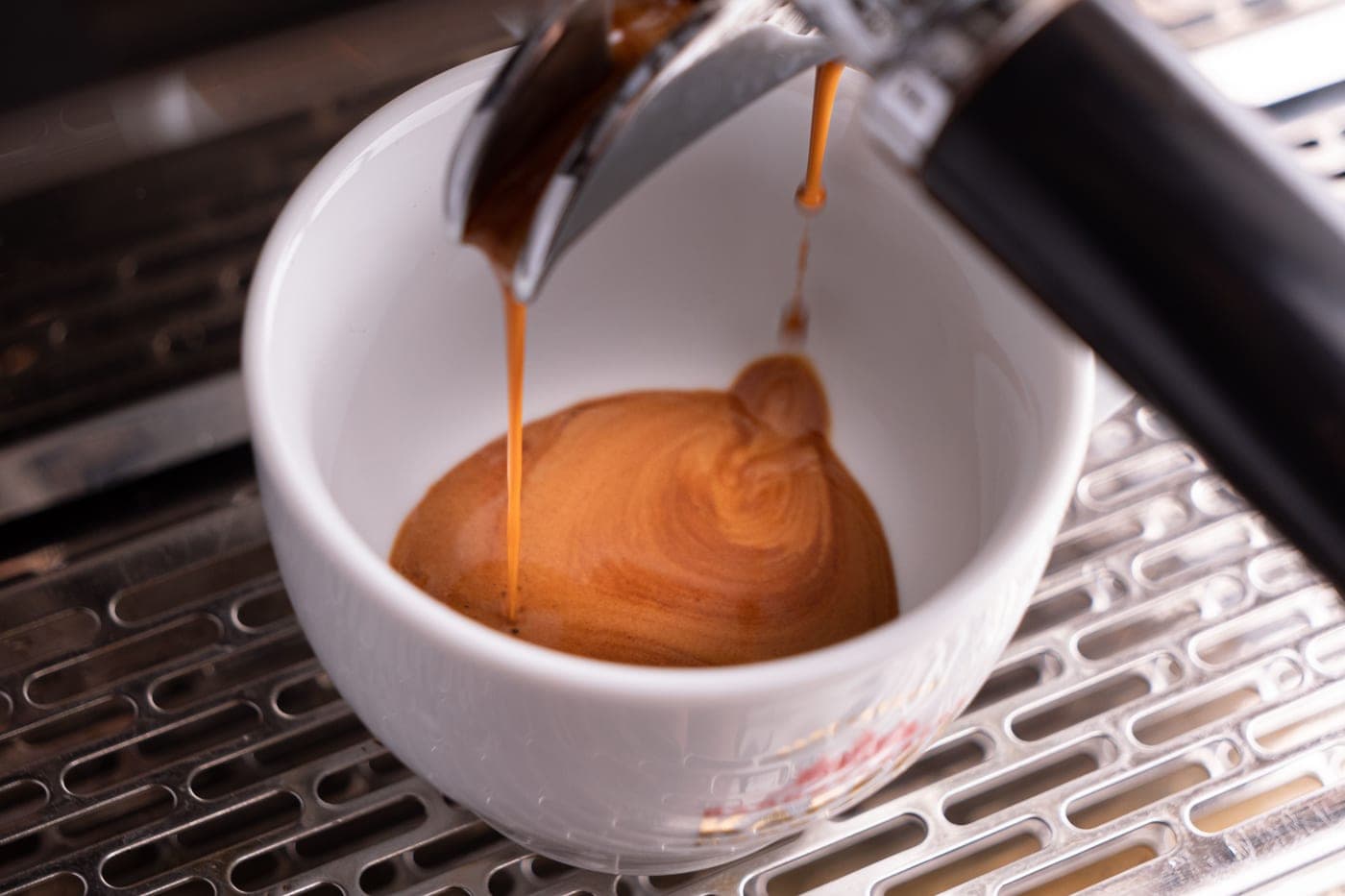 An espresso machine pulling a shot into a cup, fresh crema forming, in warm kitchen light